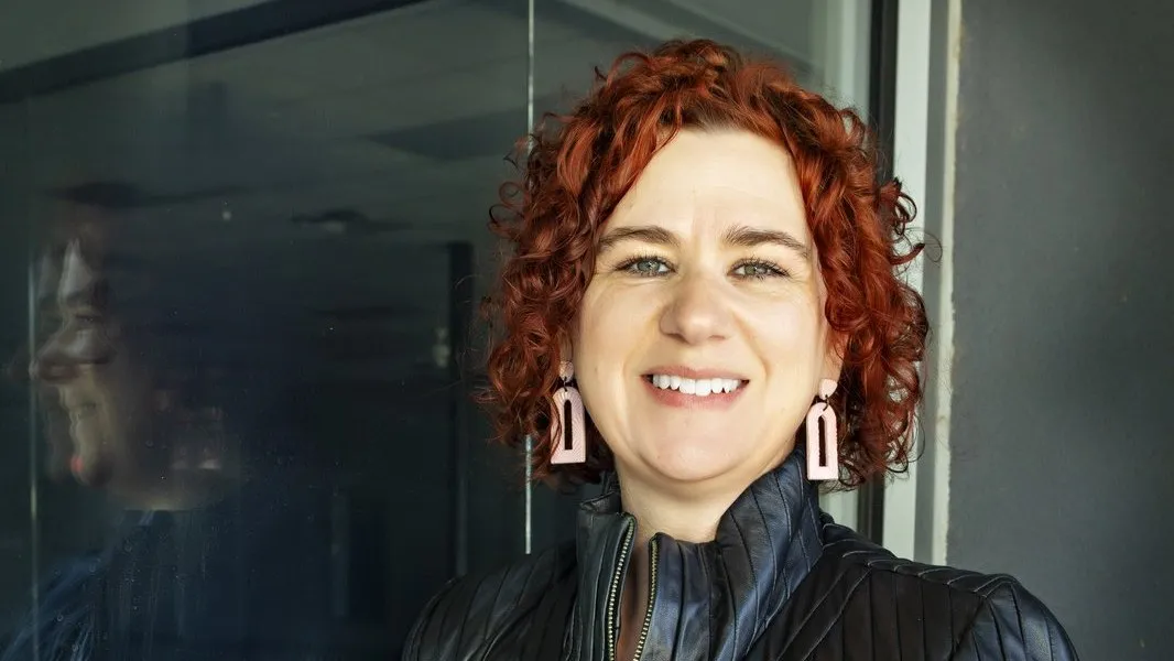 Kimberly Evans smiling in a black leather jacket beside a glass wall