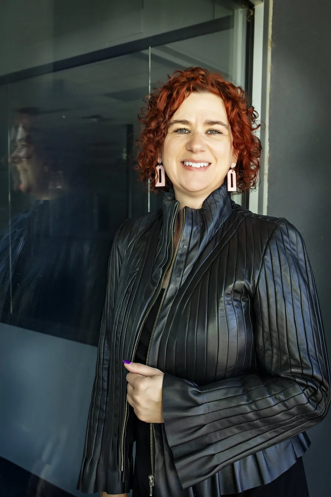 Kimberly Evans smiling in a black leather jacket beside a glass wall